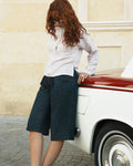 shorouqmazrawi indigo denim jorts with front pleats and cuffed hem worn by a woman leaning against a vintage car