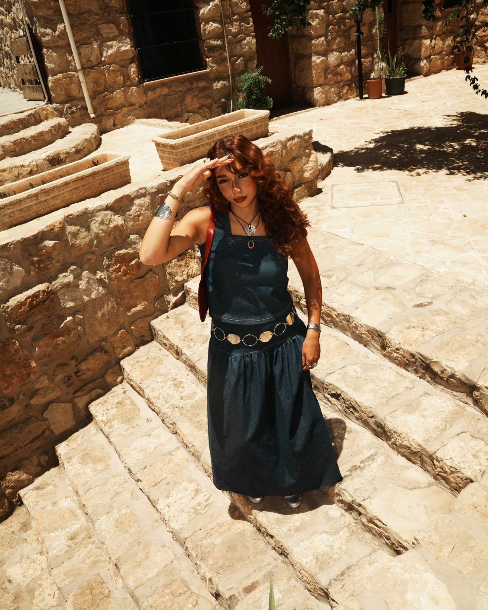 shorouqmazrawi indigo denim square-neck top with contrast stitching and side slits worn by a woman on stone steps