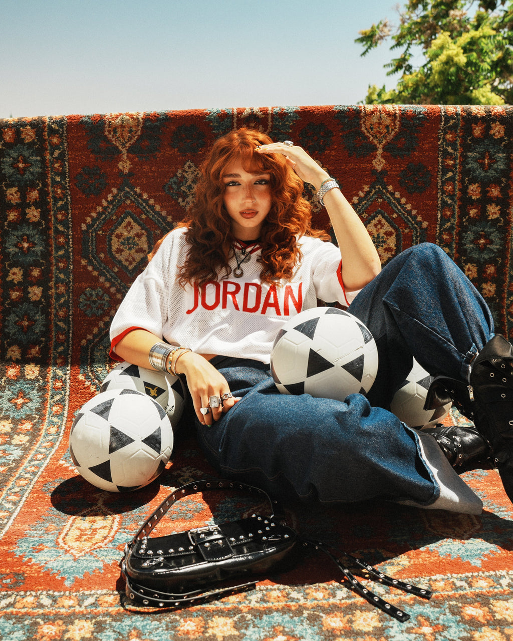 shorouqmazrawi wide-leg indigo denim pants with cuffed hems worn by a model sitting on a patterned rug with soccer balls
